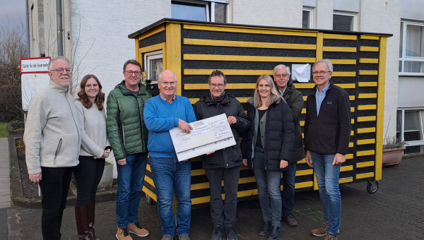 Eine Gruppe von 8 Menschen halten einen symbolischen Scheck in Händen