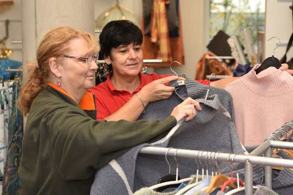 Zwei Frauen betrachten gemeinsam Kleidungsstücke an einer Kleiderstange