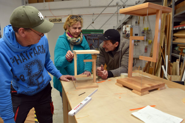 Drei Personen arbeiten gemeinsam an einem Holzprojekt in einer Werkstatt