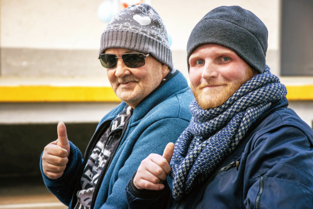 Zwei Menschen in Winterkleidung lächeln und zeigen Daumen hoch